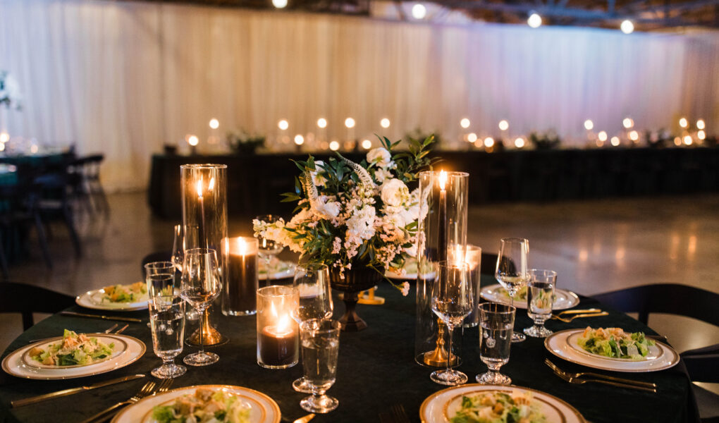 Photo of a wedding table with velvet green linens, black candles, pre-set salad, and white flowers.