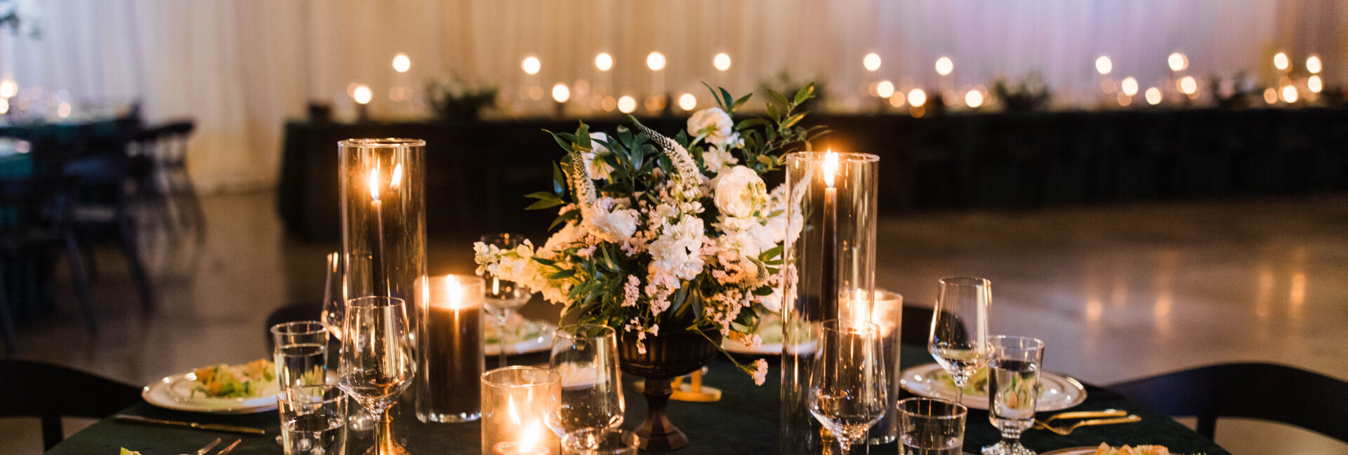 Photo of a wedding table with velvet green linens, black candles, pre-set salad, and white flowers.