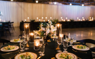 Photo of a wedding table with velvet green linens, black candles, pre-set salad, and white flowers.