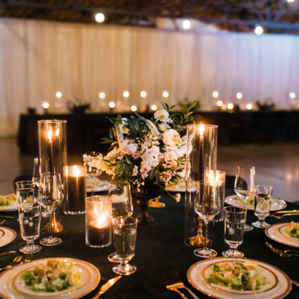 Photo of a wedding table with velvet green linens, black candles, pre-set salad, and white flowers.