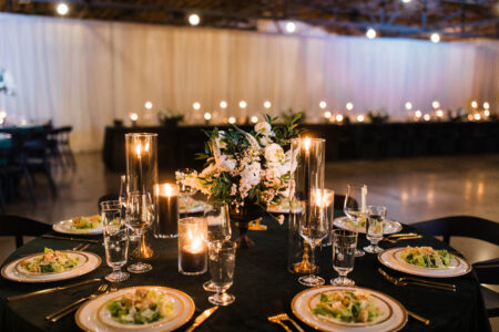 Photo of a wedding table with velvet green linens, black candles, pre-set salad, and white flowers.